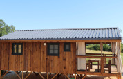Cabaña de madera con techo metálico y porche cubierto, con ventanas y terraza en un lodge rural.