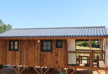 Cabaña de madera con techo metálico y porche cubierto, con ventanas y terraza en un lodge rural.