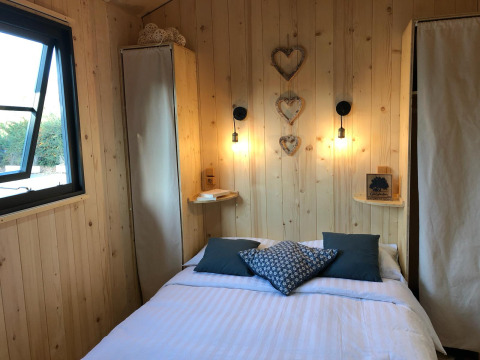 Gemütliches Schlafzimmer mit Holzvertäfelung, Doppelbett, Fenstern und herzförmigen Wanddekoren.