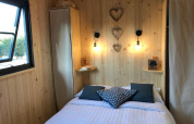 Gemütliches Schlafzimmer mit Holzvertäfelung, Doppelbett, Fenstern und herzförmigen Wanddekoren.
