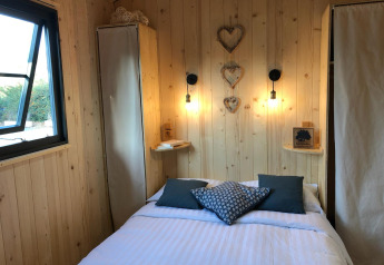 Accogliente camera di un lodge con pareti in legno, letto matrimoniale, finestra aperta e decorazioni a cuore.