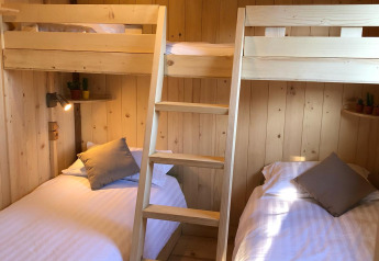 Acogedora habitación de albergue con cuatro camas tipo litera, rodeadas de paredes de madera clara.