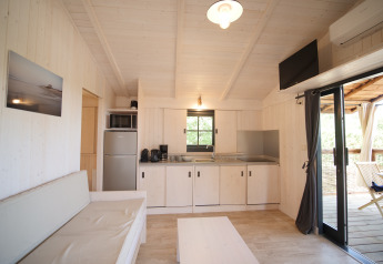 Lyst, moderne lodge-interiør med tekøkken, sofa, bord, tv, aircondition og udsigt til træterrasse.