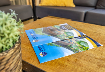 Due brochure di tende safari su un tavolo di legno, con una pianta a sinistra e un divano sullo sfondo.
