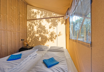 Camera accogliente in una tenda safari con due letti singoli, asciugamani blu e luce naturale abbondante.