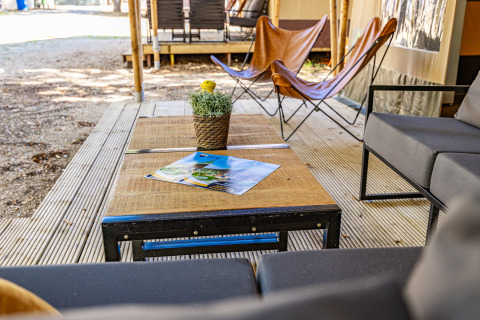 Outdoor-Loungebereich an einem Safarizelt mit modernen Möbeln, Holztisch und Pflanze auf der Terrasse.