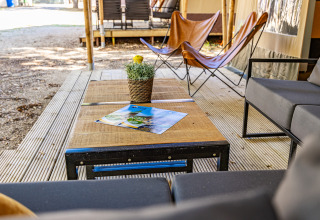 Buitenlounge bij een safaritent met moderne meubels, houten tafel en een plantje op het terras.