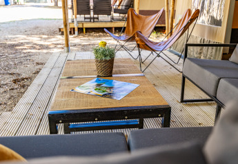 Outdoor lounge area at a safari tent with modern furniture, wooden table, and potted plant on the patio.