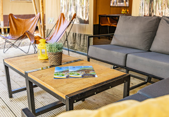 Area lounge esterna in tenda safari con sedute moderne, tavolini in legno e piante decorative.