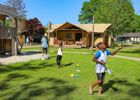 Kinderen en volwassenen genieten van buitenspelen en ontspanning bij een luxe glamping tent op een vakantiepark.