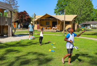 Kinderen en volwassenen genieten van buitenspelen en ontspanning bij een luxe glamping tent op een vakantiepark.