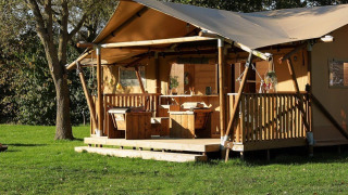 Tienda glamping La Vida con terraza de madera y mesa de picnic en un entorno verde y arbolado.