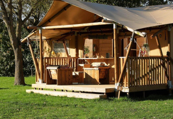 Glamping telt La Vida med træterrasse og picnicbord i en grøn, solrig skovomgivelse.