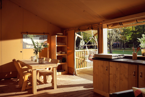 Vista interior de una lujosa tienda glamping safari con muebles de madera, cocina y vista a la naturaleza.