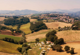 Vista aérea del camping Suasa en Marche, Italia, rodeado de campos dorados y colinas pintorescas.