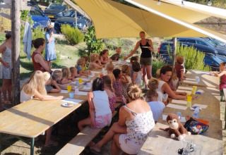 Bambini e adulti partecipano a un laboratorio all'aperto sotto un telo al Camping Suasa nelle Marche, Italia.