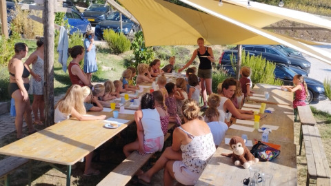 Børn og voksne deltager i en udendørs workshop under en teltdug på Camping Suasa i Marche, Italien.