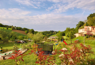 Panorama al Camping Suasa nelle Marche, Italia, con area giochi, trampolino e campagna verde sotto cielo azzurro.
