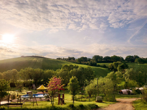 Panoramic view of Camping Suasa holiday park in Marche, Italy, showing hills, trees, a pool, and tents at sunset.