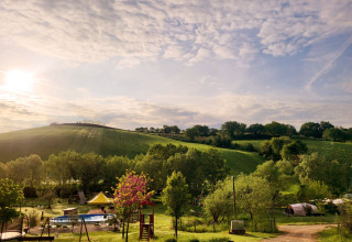 Panoramic view of Camping Suasa holiday park in Marche, Italy, showing hills, trees, a pool, and tents at sunset.