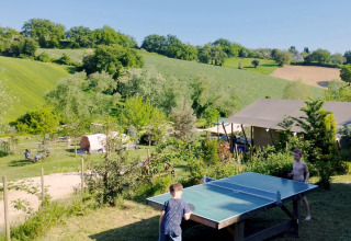 Due bambini giocano a ping pong all'aperto al Camping Suasa, circondati dalle colline verdi delle Marche, Italia.