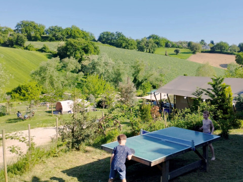 Due bambini giocano a ping pong all'aperto al Camping Suasa, circondati dalle colline verdi delle Marche, Italia.