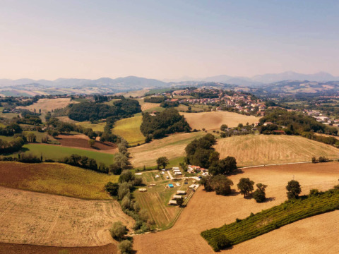 Aerial view of Camping Suasa holiday park nestled among hills and fields in Marche, Italy, on a sunny day.