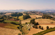 Luchtfoto van Camping Suasa vakantiepark te midden van heuvels en velden in Marche, Italië, op een zonnige dag.