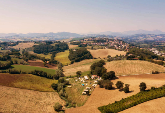 Vue aérienne du Camping Suasa au cœur des collines et champs de la région des Marches, en Italie, par beau temps.