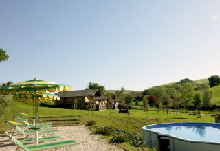 View of Camping Suasa in Marche, Italy, featuring a pool, loungers, umbrellas, and scenic green hills.