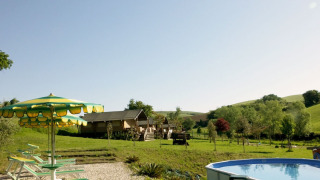View of Camping Suasa in Marche, Italy, featuring a pool, loungers, umbrellas, and scenic green hills.