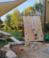 Kinderen spelen op een klimwand en in een zandbak onder schaduwdoeken bij Camping Suasa in Italië.