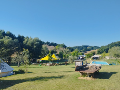 Camping Suasa vakantiepark in Marche, Italië, met tenten, groene heuvels, speeltuin en blauwe lucht.