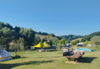 Camping Suasa holiday park in Marche, Italy, showing tents, green landscape, playground, and blue sky.