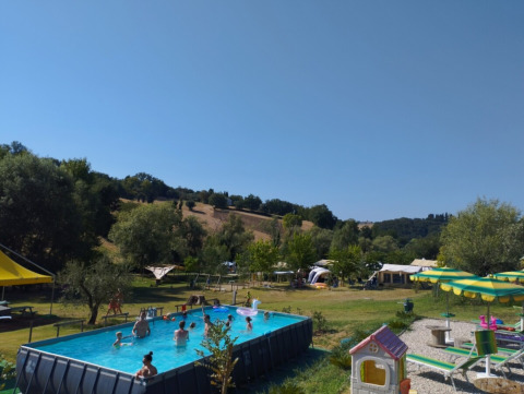 Camping Suasa holiday park in Marche, Italy, featuring a pool with kids swimming and tents in the background.