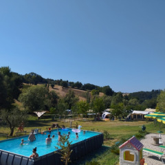 Camping Suasa holiday park in Marche, Italy, featuring a pool with kids swimming and tents in the background.