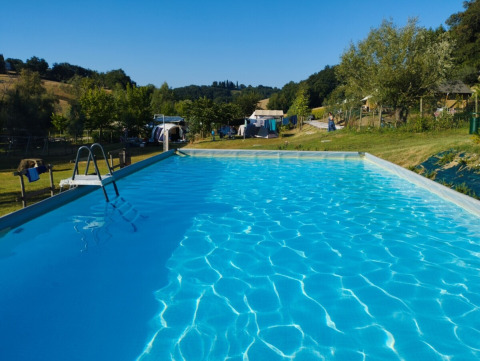 Outdoor swimming pool at Camping Suasa holiday park in Marche, Italy, surrounded by greenery and tents.