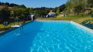 Outdoor swimming pool at Camping Suasa holiday park in Marche, Italy, surrounded by greenery and tents.