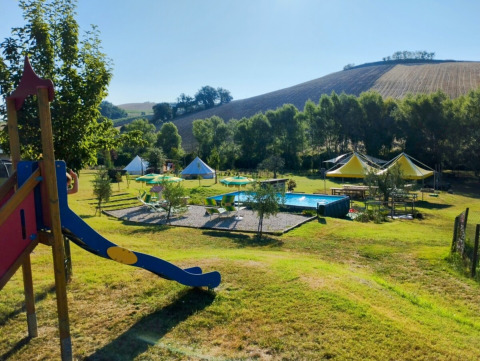 Area giochi e piscina circondate da colline e verde al Camping Suasa, parco vacanze nelle Marche, Italia.