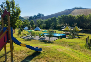 Aire de jeux et piscine dans un cadre vallonné et verdoyant au Camping Suasa, parc de vacances dans les Marches, Italie.