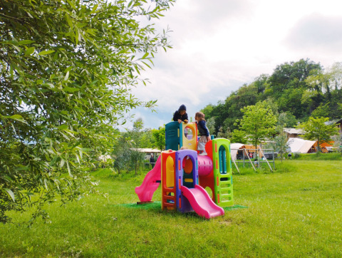 Children playing on a colorful playground surrounded by grass at Camping Suasa holiday park, Marche, Italy.