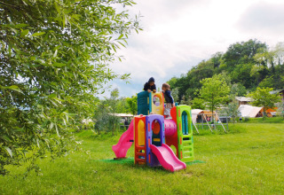 Children playing on a colorful playground surrounded by grass at Camping Suasa holiday park, Marche, Italy.