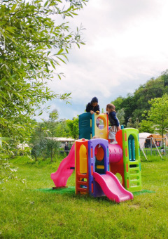 Children playing on a colorful playground surrounded by grass at Camping Suasa holiday park, Marche, Italy.