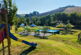 Camping Suasa parque de vacaciones en Marche, Italia, con área de juegos, piscina, tiendas y colinas.