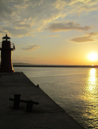 Sunset over the sea with a lighthouse on a pier near Castelleone di Suasa, Marche, Italy.