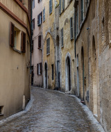 Narrow cobblestone street with old buildings and shutters near Castelleone di Suasa, Marche, Italy.