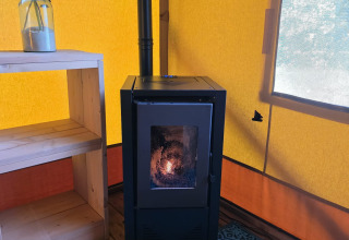 Interior de una tienda glamping safari con estufa negra, pared amarilla y alfombra azul en Resort de Parel.