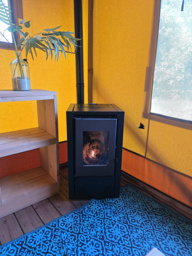 Interior of a safari glamping tent with a black stove, yellow wall, and blue rug at Resort de Parel.