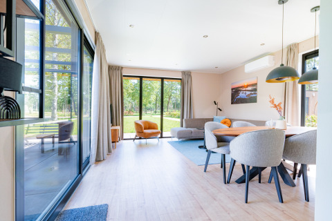 Lichte, moderne woonkamer in Vakantievilla Amalia 6 met grote ramen en uitzicht op het groene park.