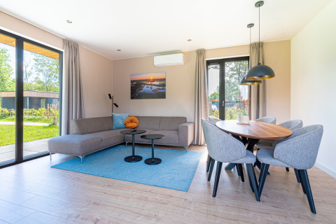 Moderne woonkamer in Vakantievilla Amalia 6 met bank, eethoek en grote ramen bij Hofparken De Bergvennen, Nederland.